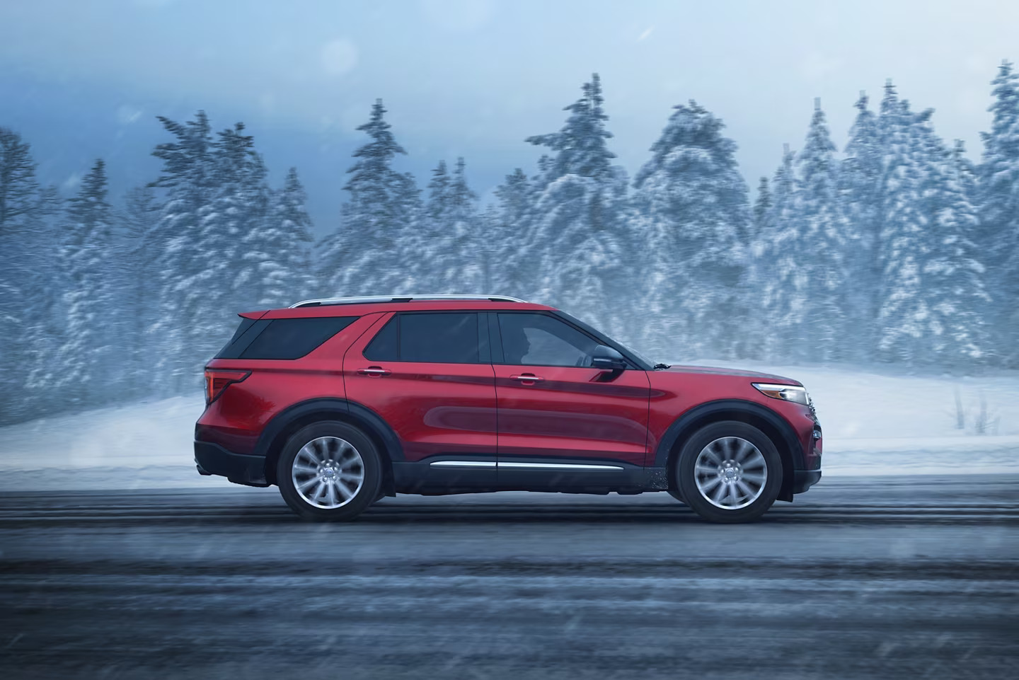 Red 2024 Ford Explorer drives down a road with snow-capped pines bordering the roadside.