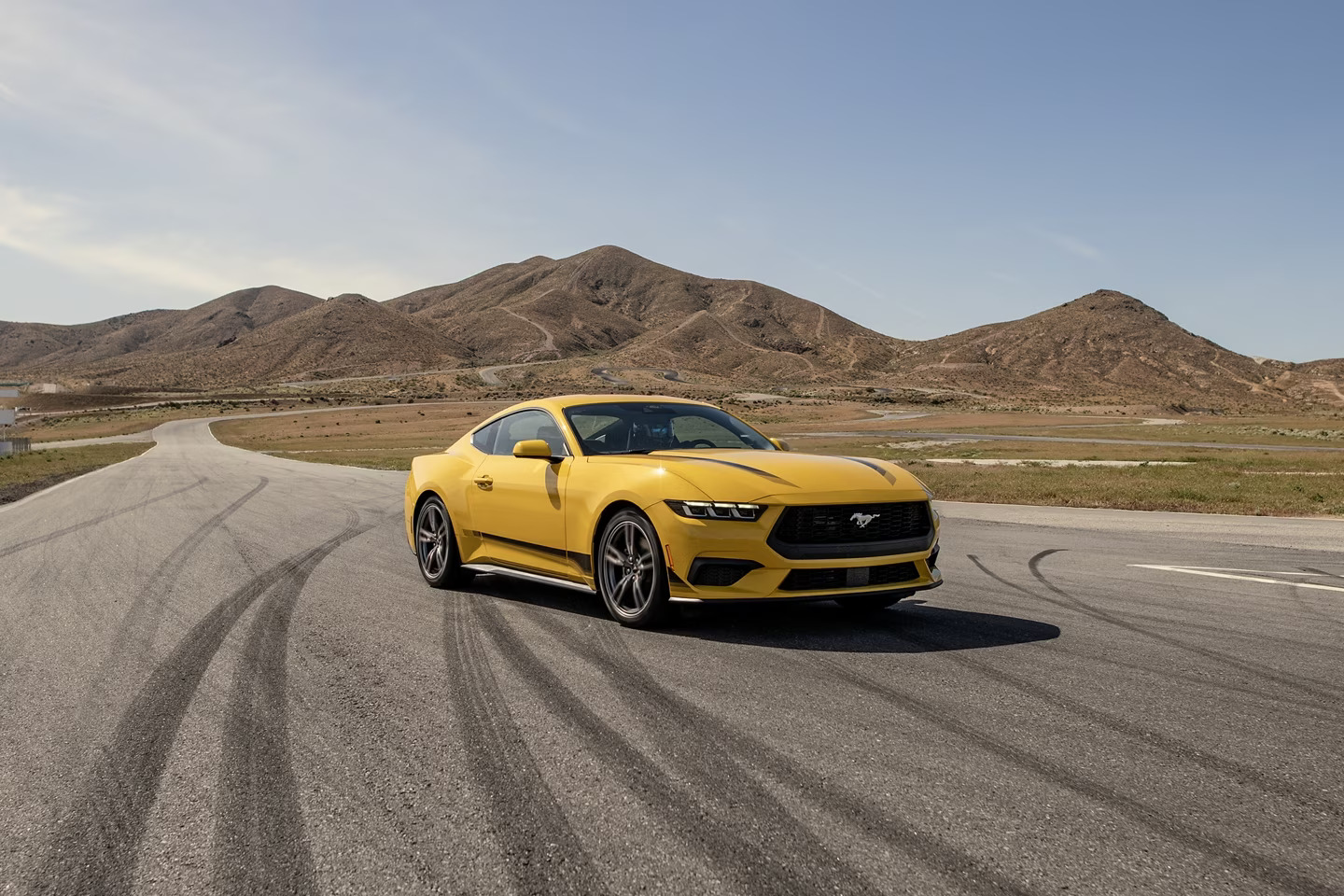 A yellow Ford mustang from Ford dealerships in Jacksonville NC sits on a road with desert hills in the background.