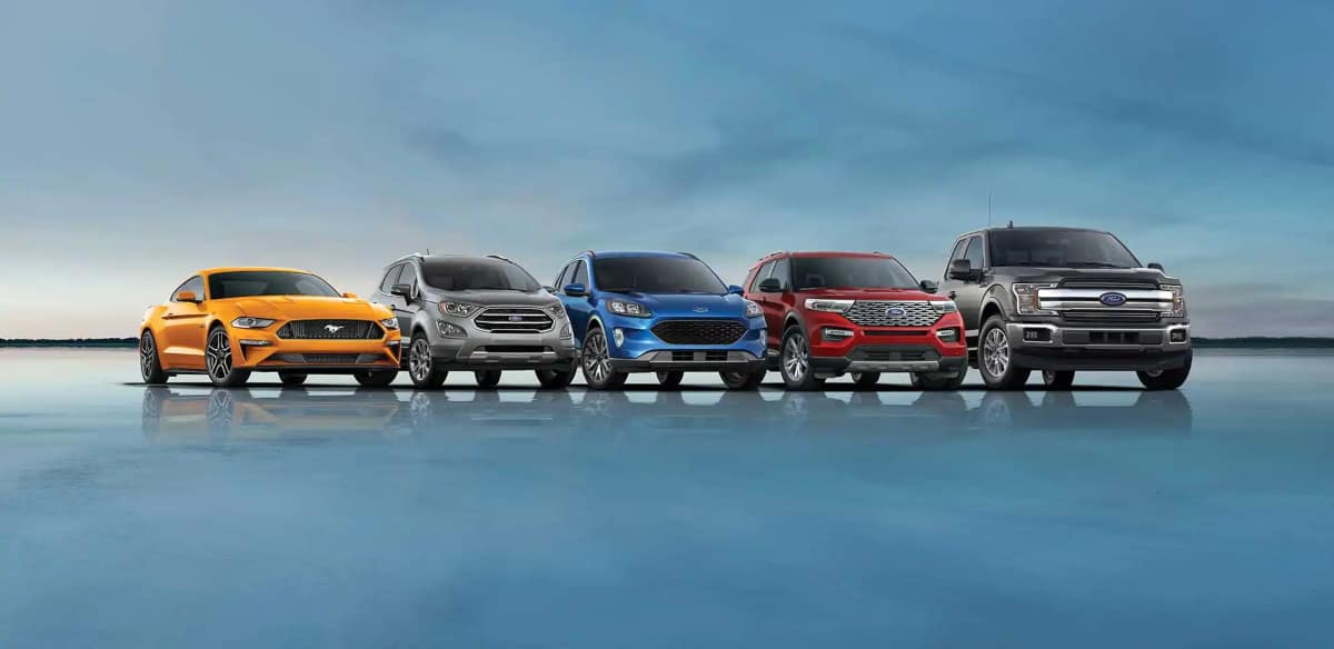 Ford SUVs, cars, and trucks are in a line against the background of the twilight sky.